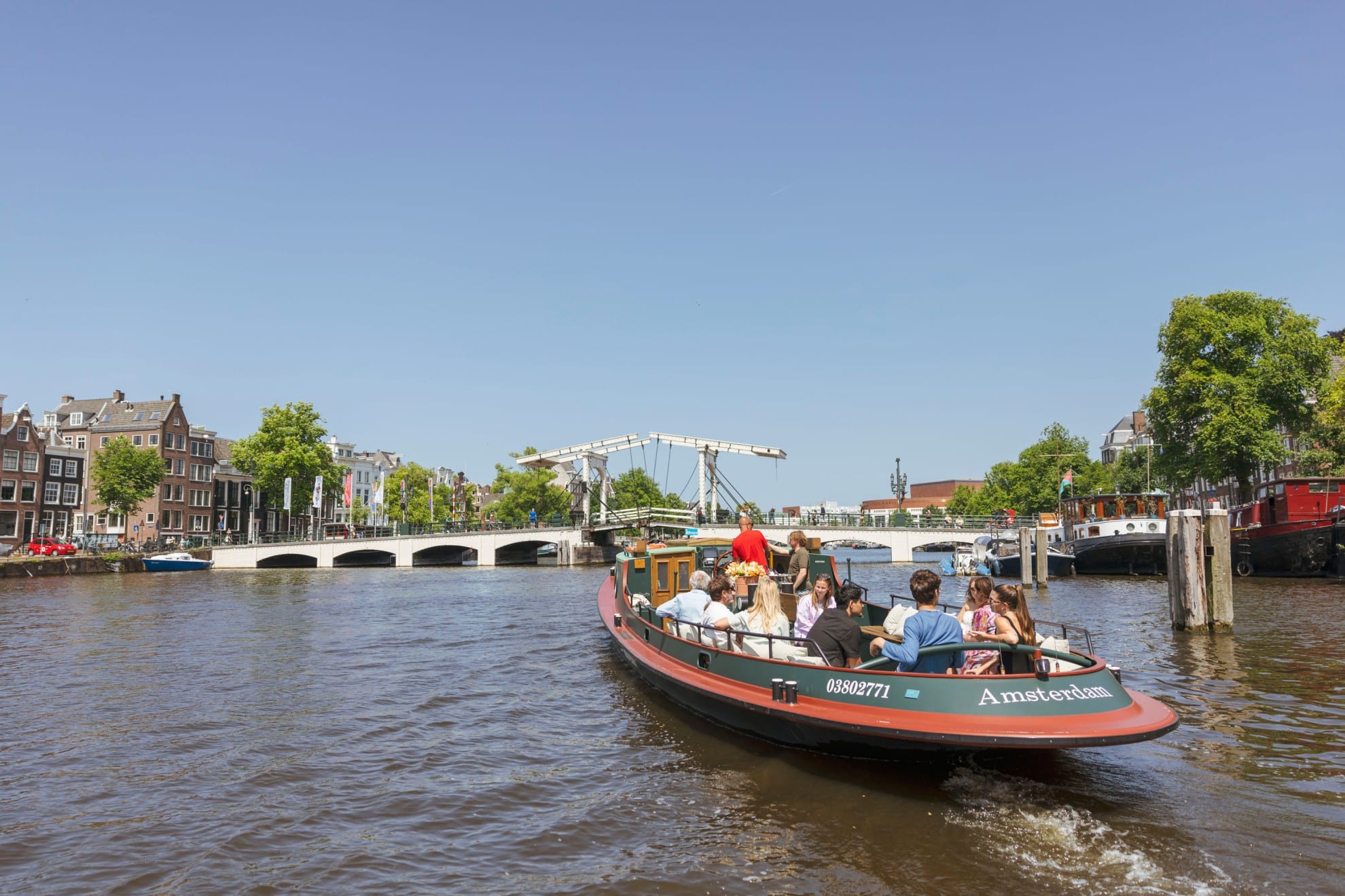 Una classica barca da crociera piena di passeggeri naviga su un canale di Amsterdam verso il Magere Brug in una giornata di sole.
